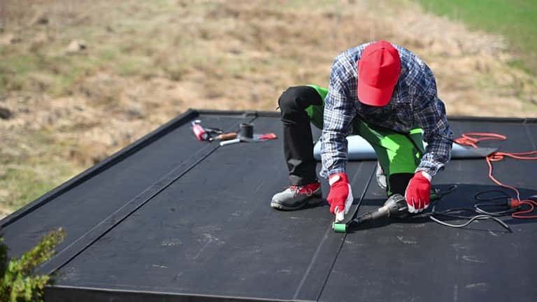 Professional Roofer Installing EPDM Rubber Roofing Membrane Using Cordless Heat Gun Tool. Construction Industry.